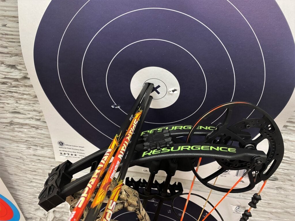 Three arrows in the bullseye of a target with a bow next to the target 