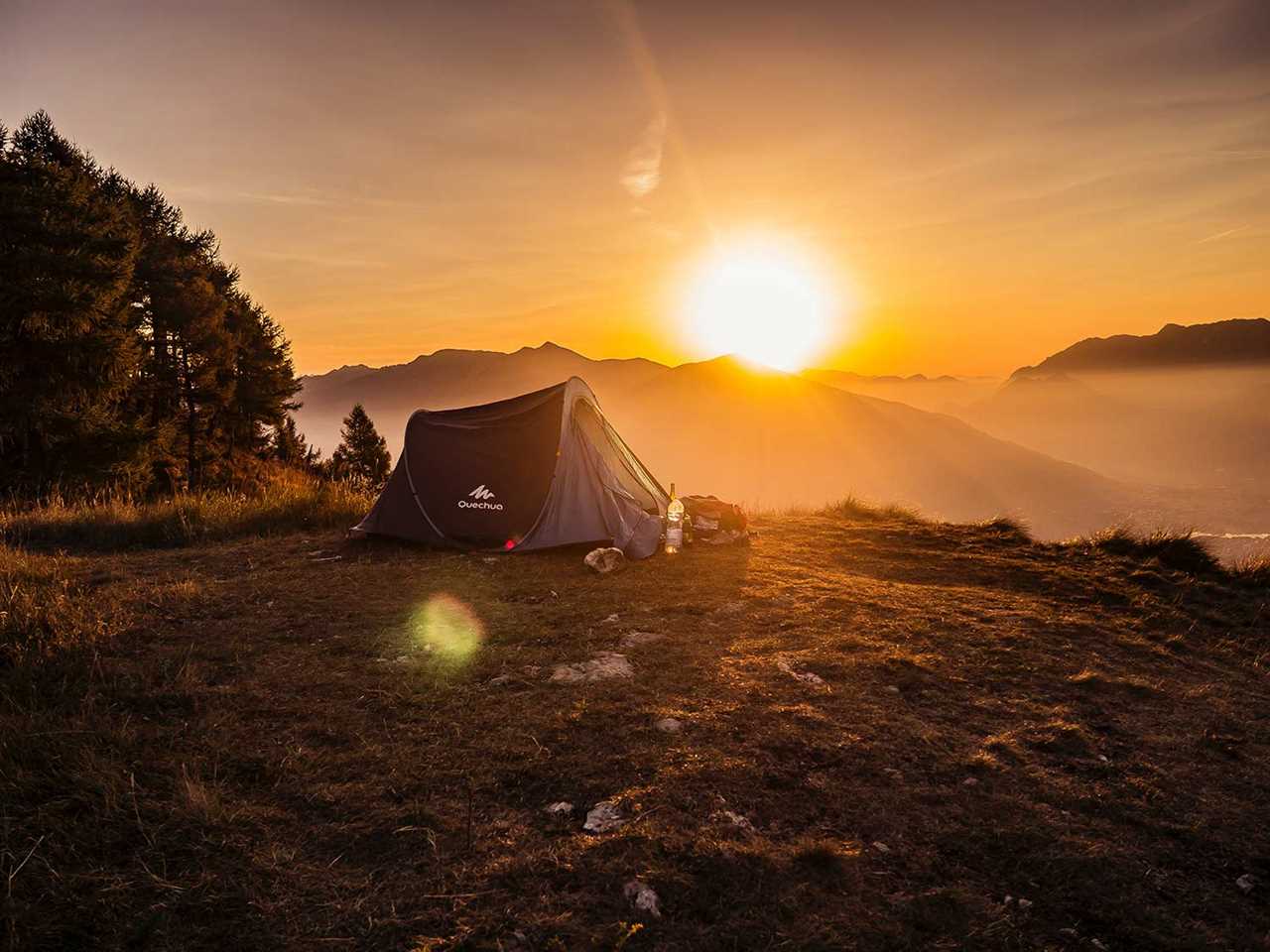 A camping tent on a hillside overlooking mountains and a sunset.