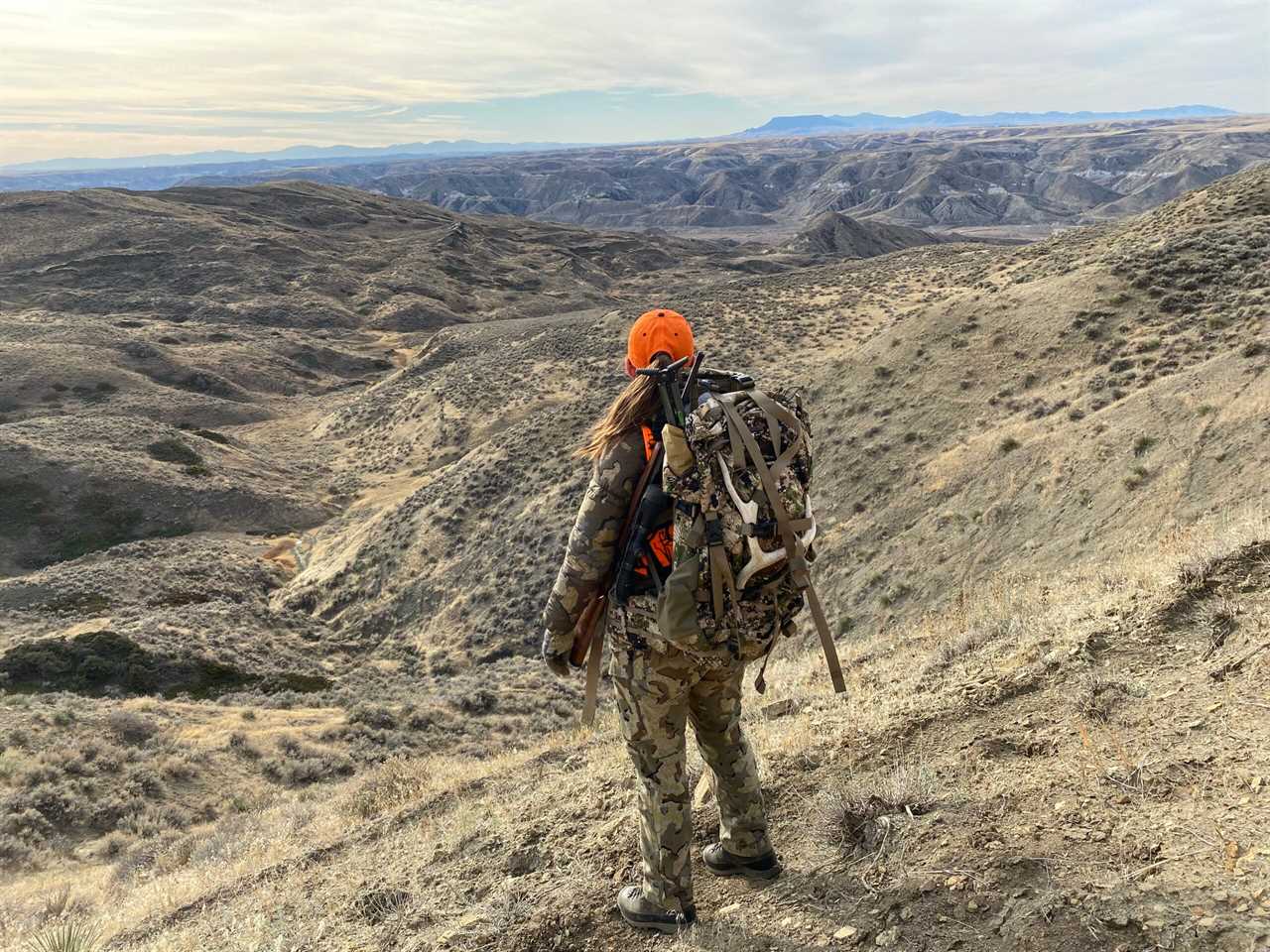 A woman in camouflage with an orange hat looking over a landscape