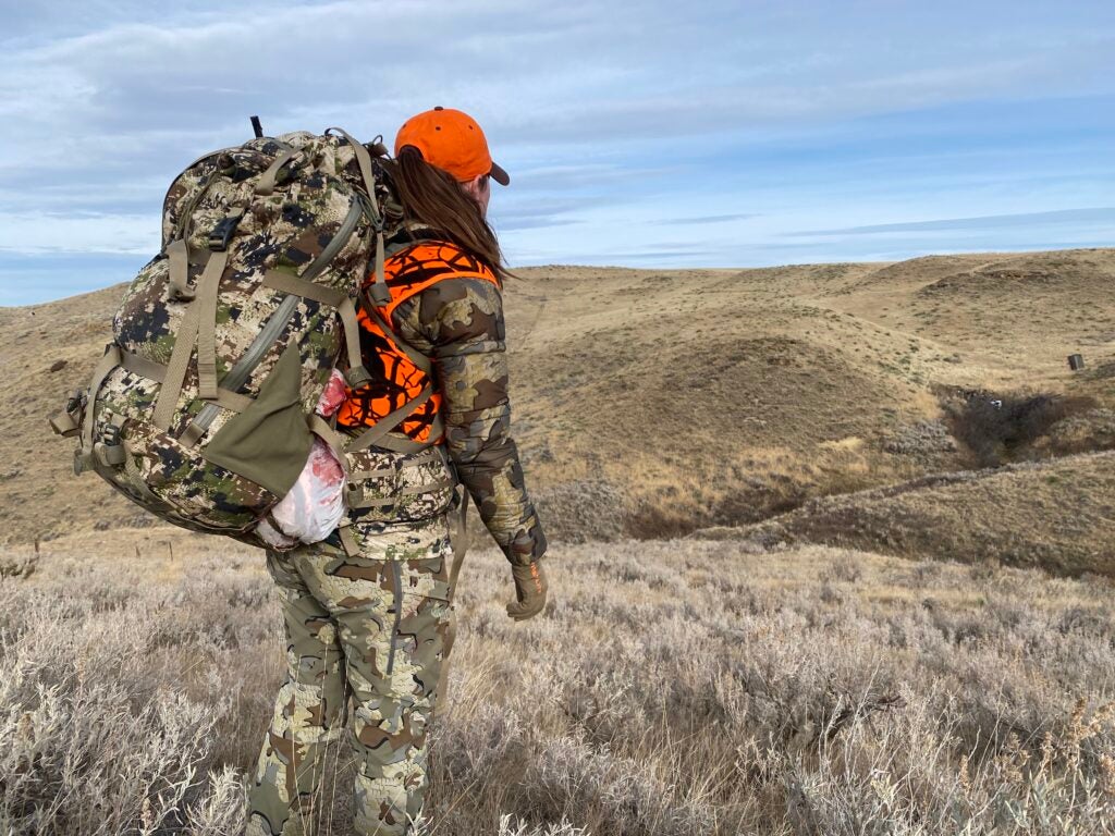 A woman wearing KUIU Women’s Super Down ULTRA Hooded Jacket in field