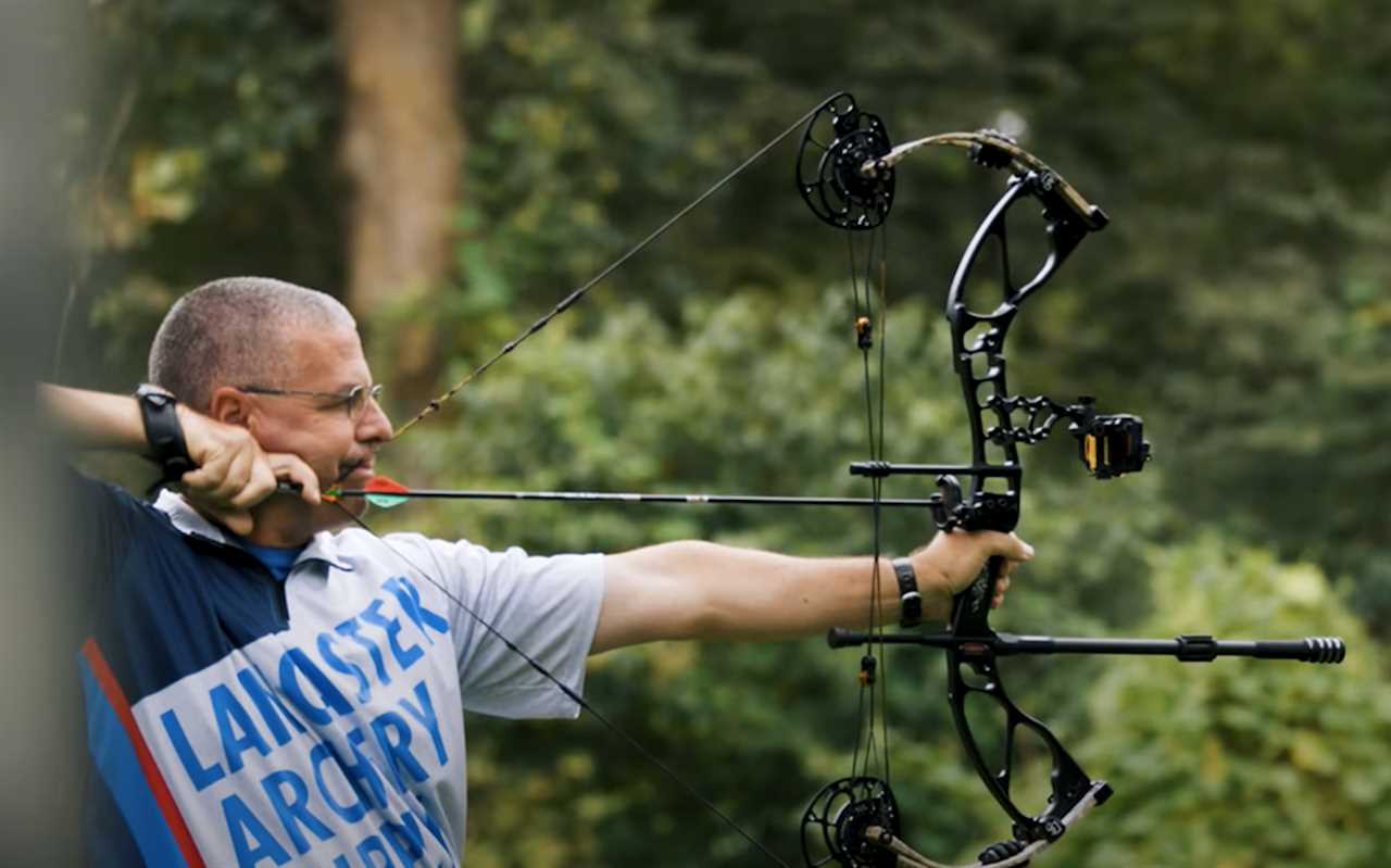 A man shooting a black bow in the woods