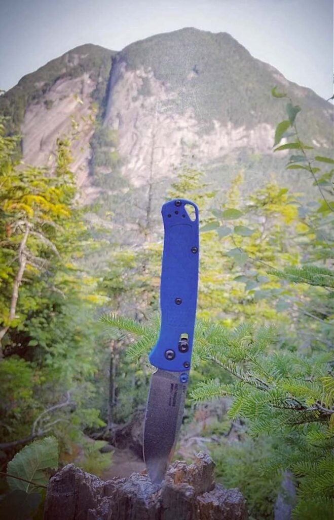 A silver and blue best folding knife in a rock with a mountain in the background