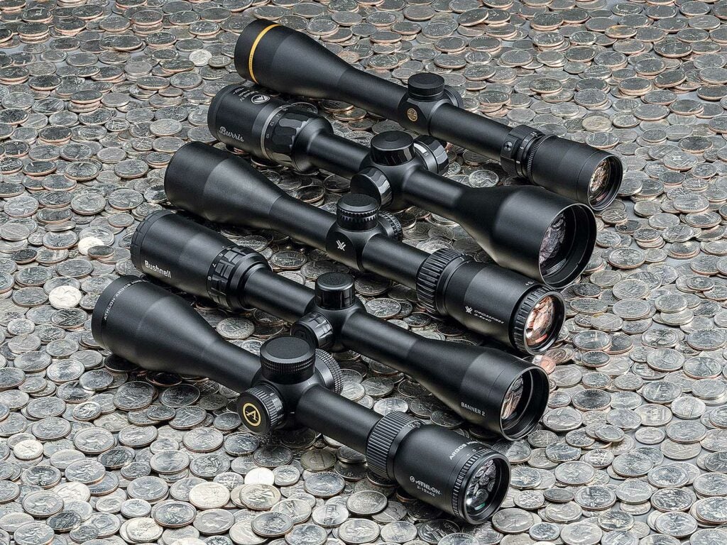 Five riflescopes lined up and arranged on a pile of quarters.