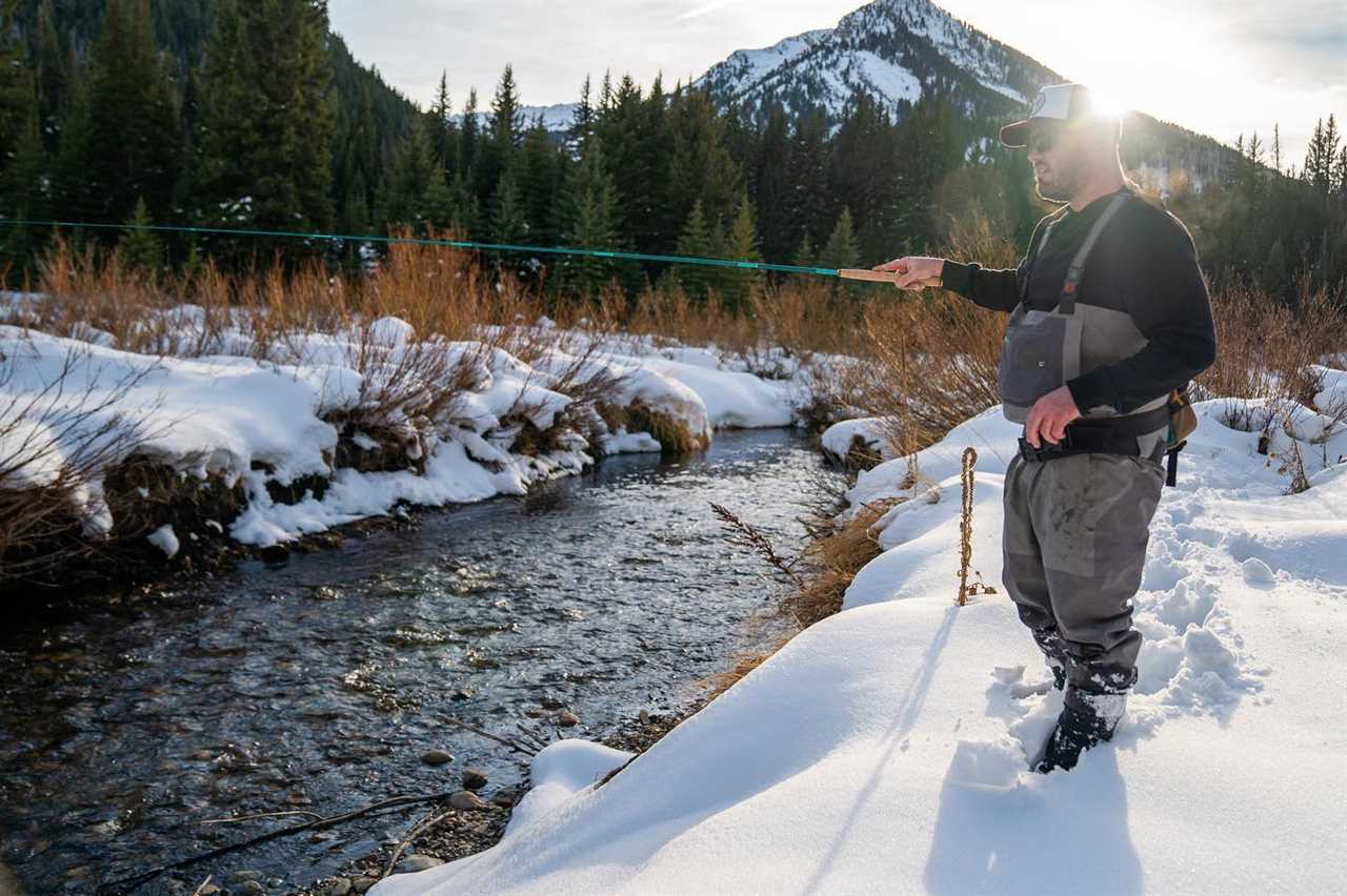 A man fishing with a tenkara rod on a snowy river bank