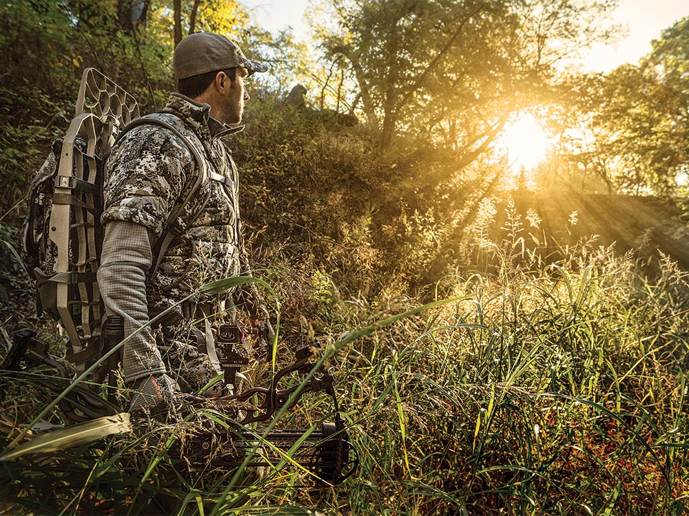 bow hunter hiking through woods