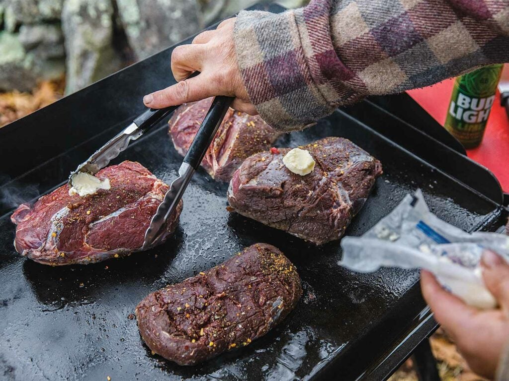 venison steaks with butter on a grill