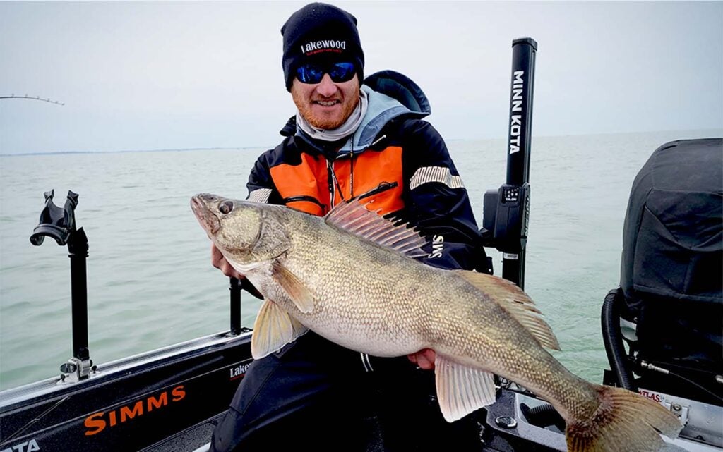 A man in an orange jacket holding a walleye on a boat