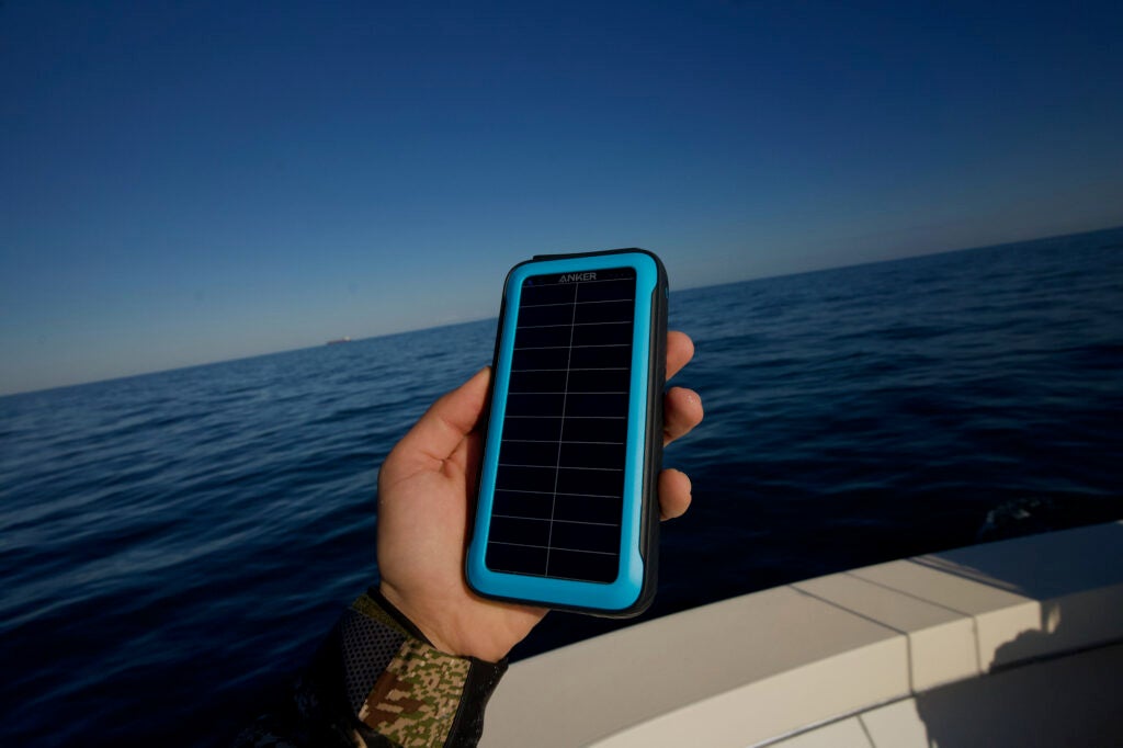 A hand holding a blue and black solar charger over the ocean