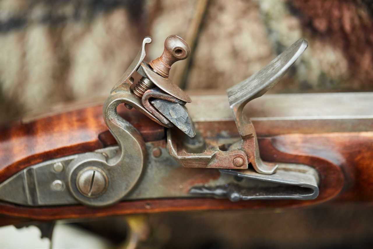 A detail of a flintlock rifle, showing the flint, flash pan, and hammer.