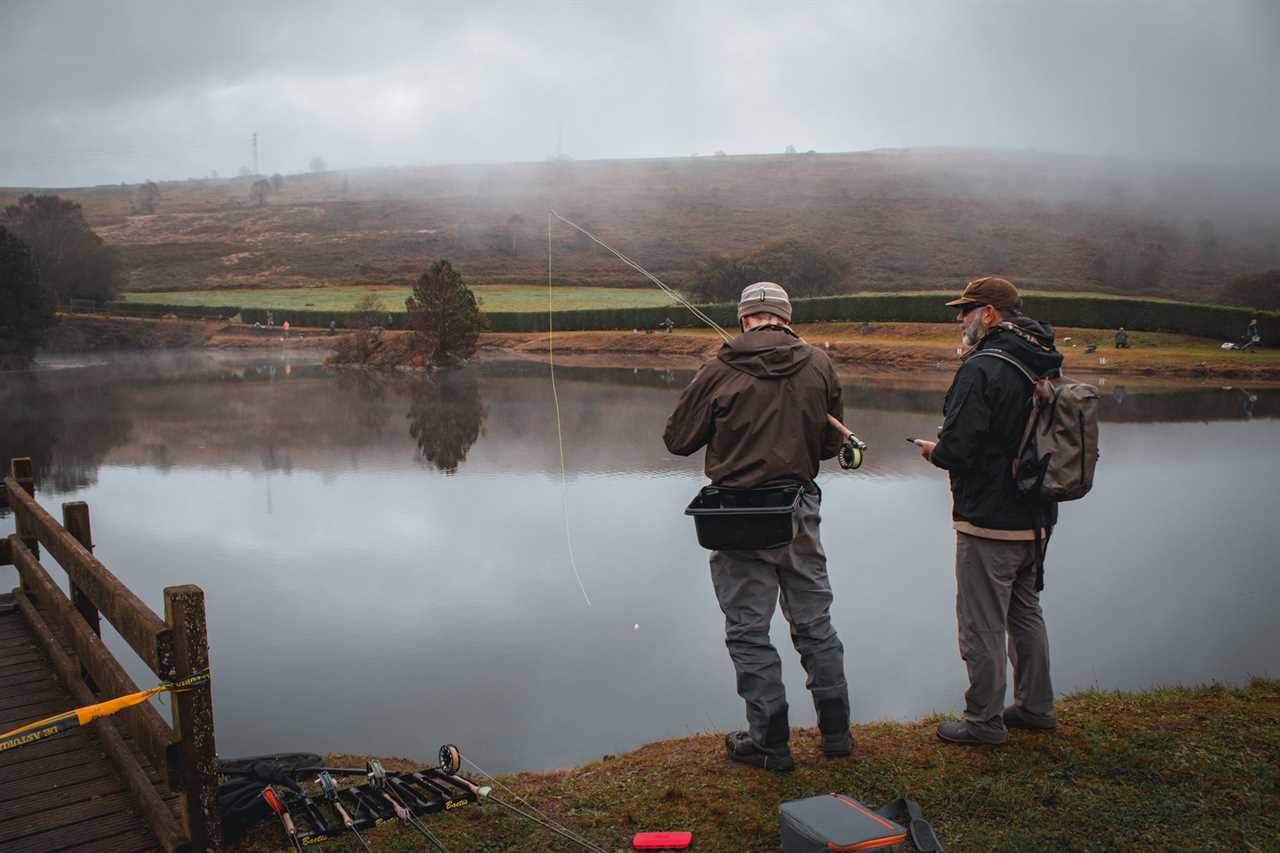 Two men stand beside a misty pond