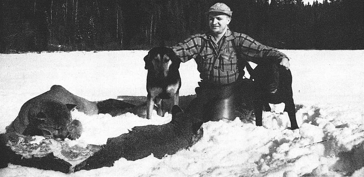 Hunter poses with two dogs and dead cougar