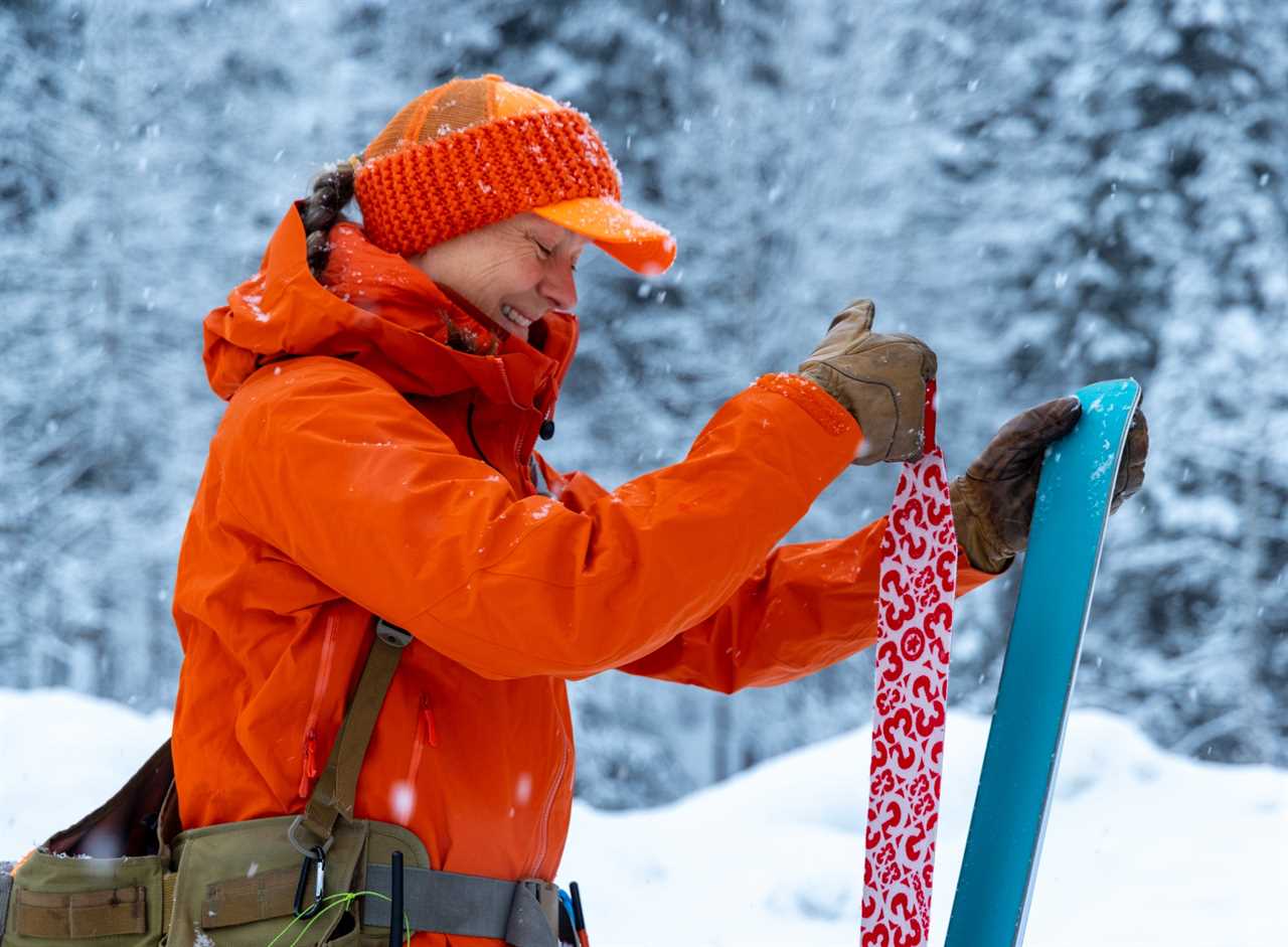 A woman in blaze orange attaches a skin to the bottom of her ski.