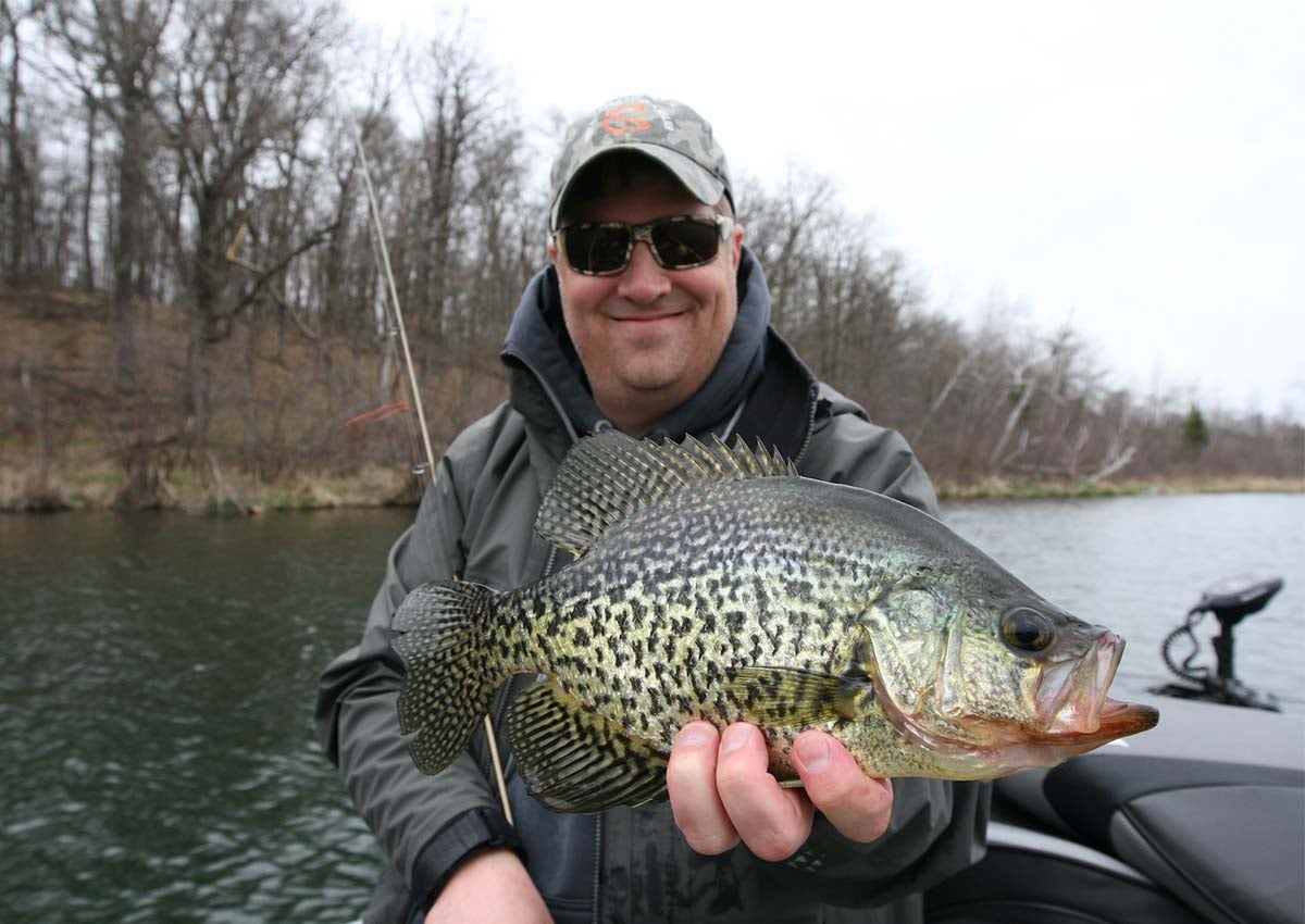 Man holding crappie and fishing rod in a boat.