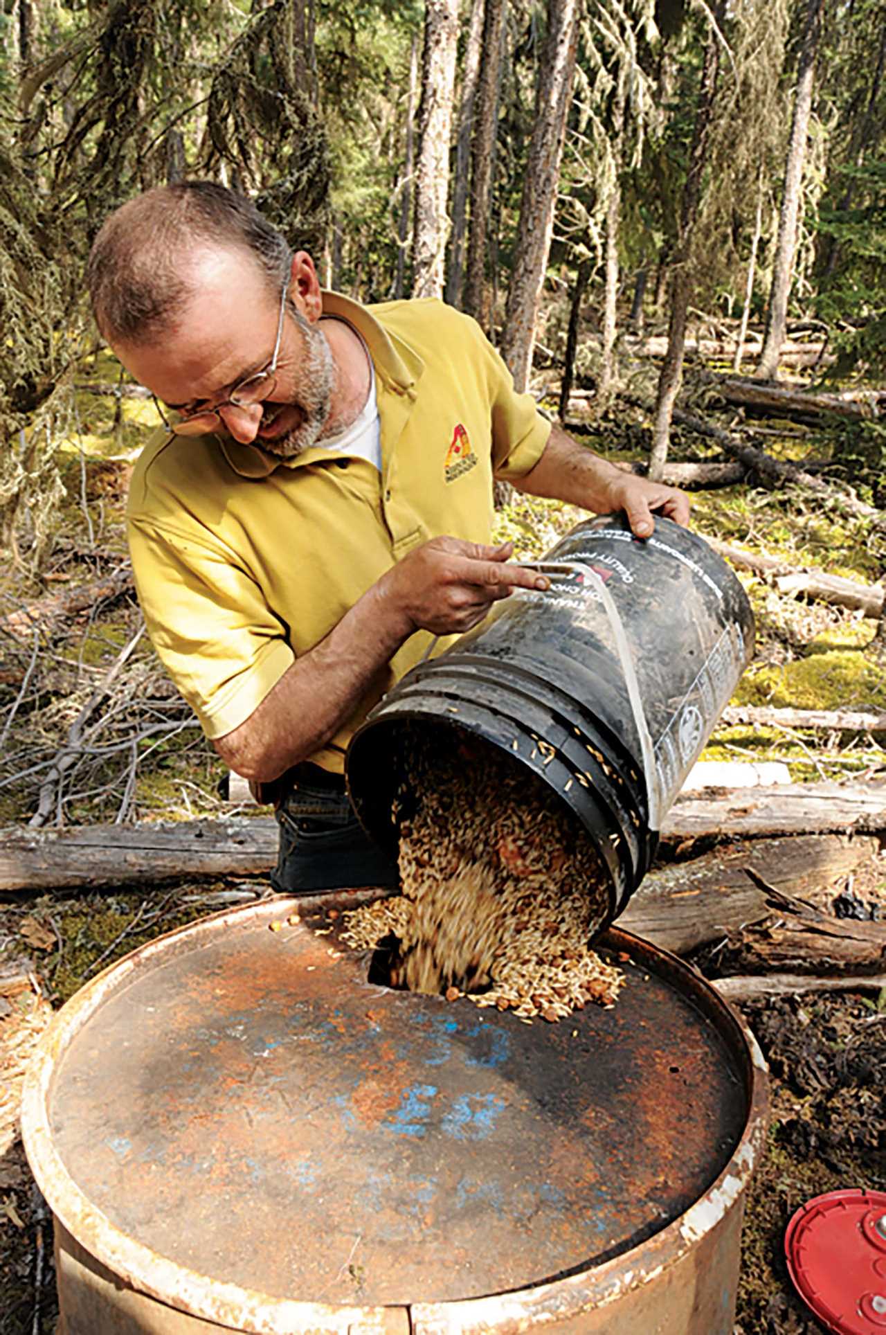 man pouring food from bucket into oil drum