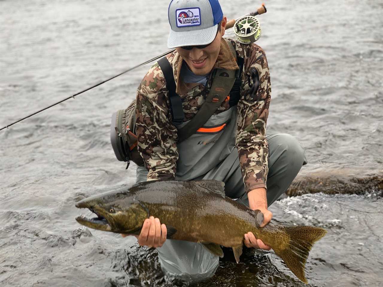 A man in the water wearing a fishing sling pack holding a large fish