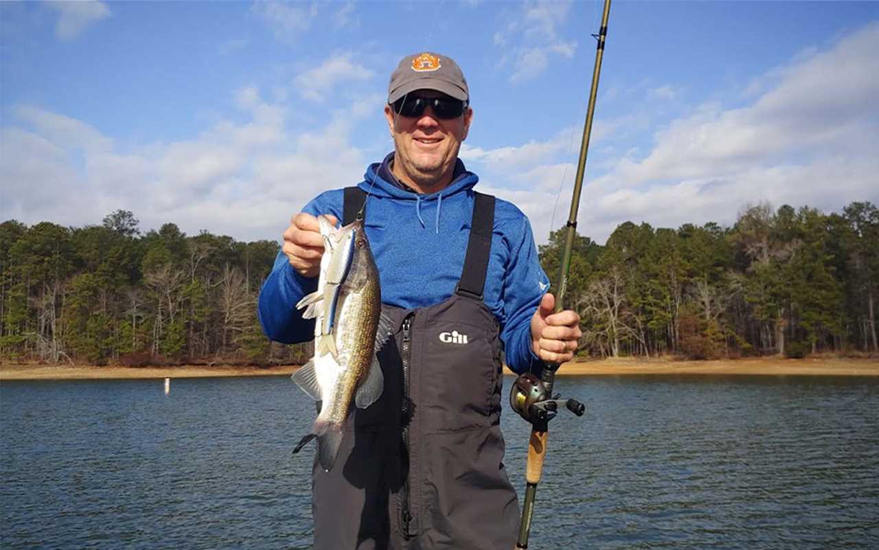 A man standing in water holding a bass and a fishing rod