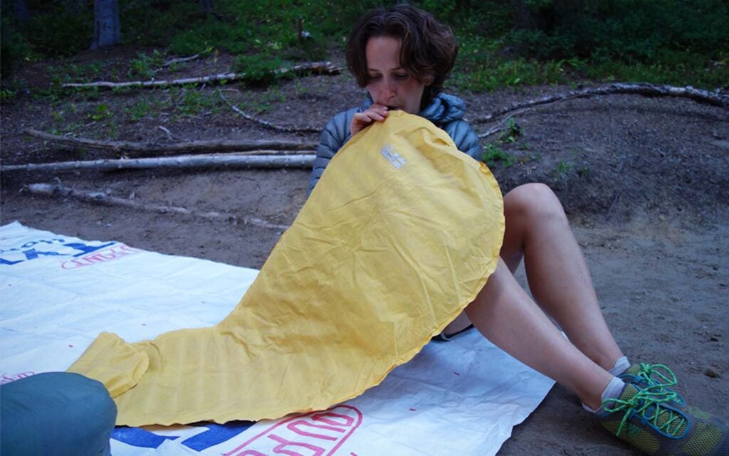 A woman blowing up a yellow sleeping pad