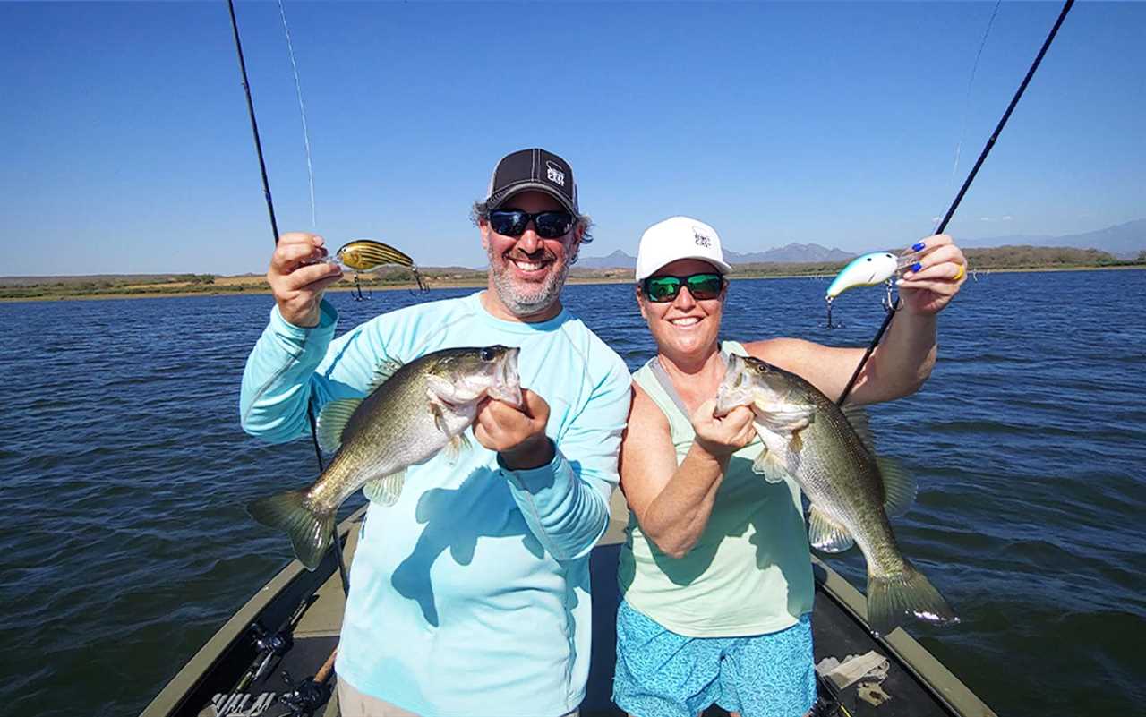 A man and a woman on a boat holding fishing rods and bass