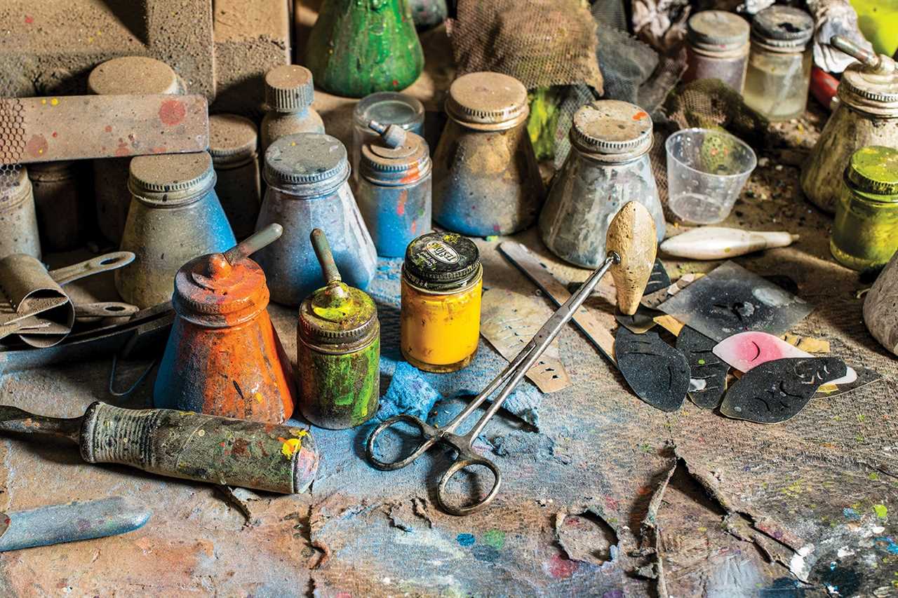 fishing lure blank rests on its end, held up by a hemostat and surrounded by paint jars, sand paper, and other tools