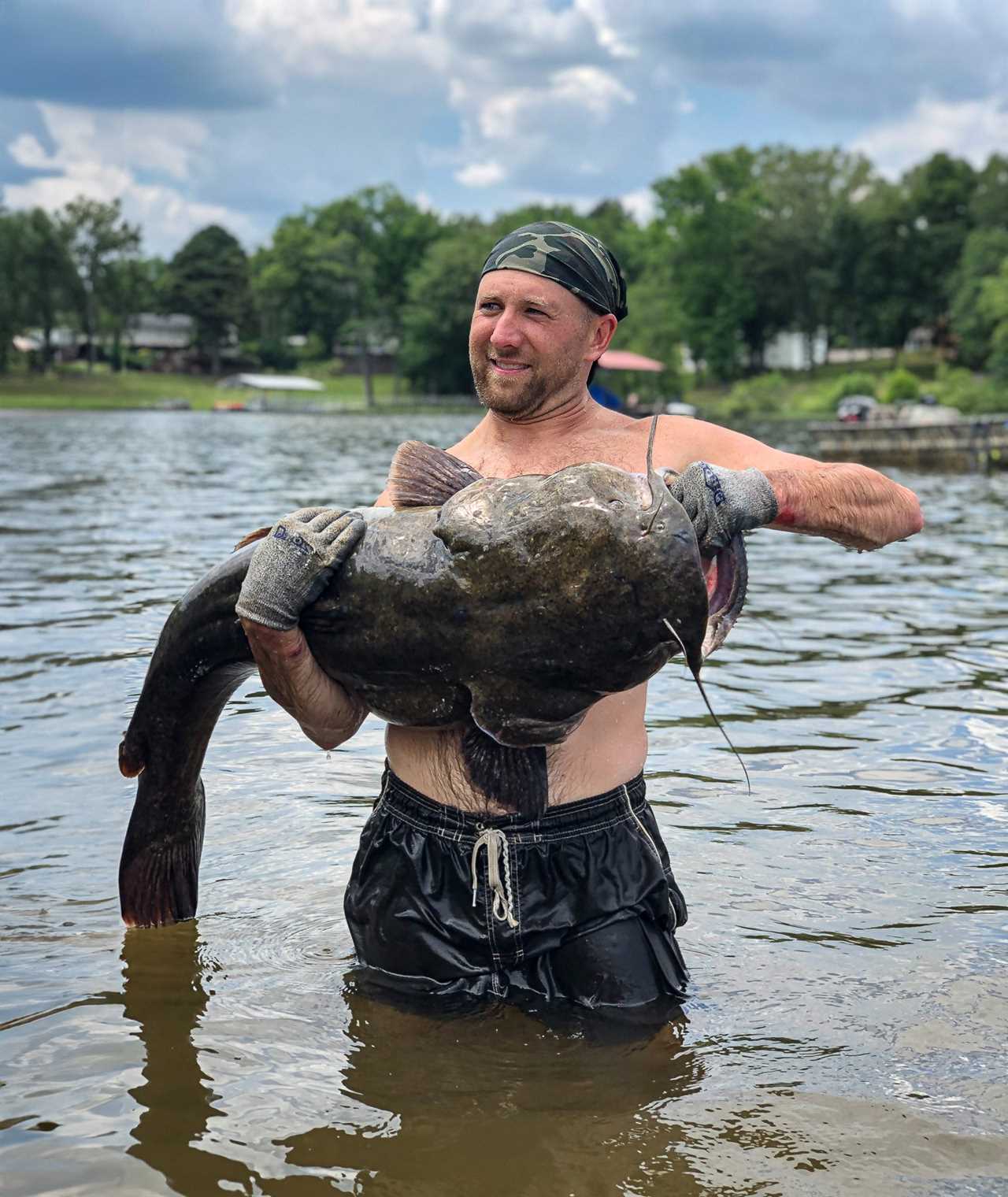 A noodler supports a heavy trophy flathead with two hands.