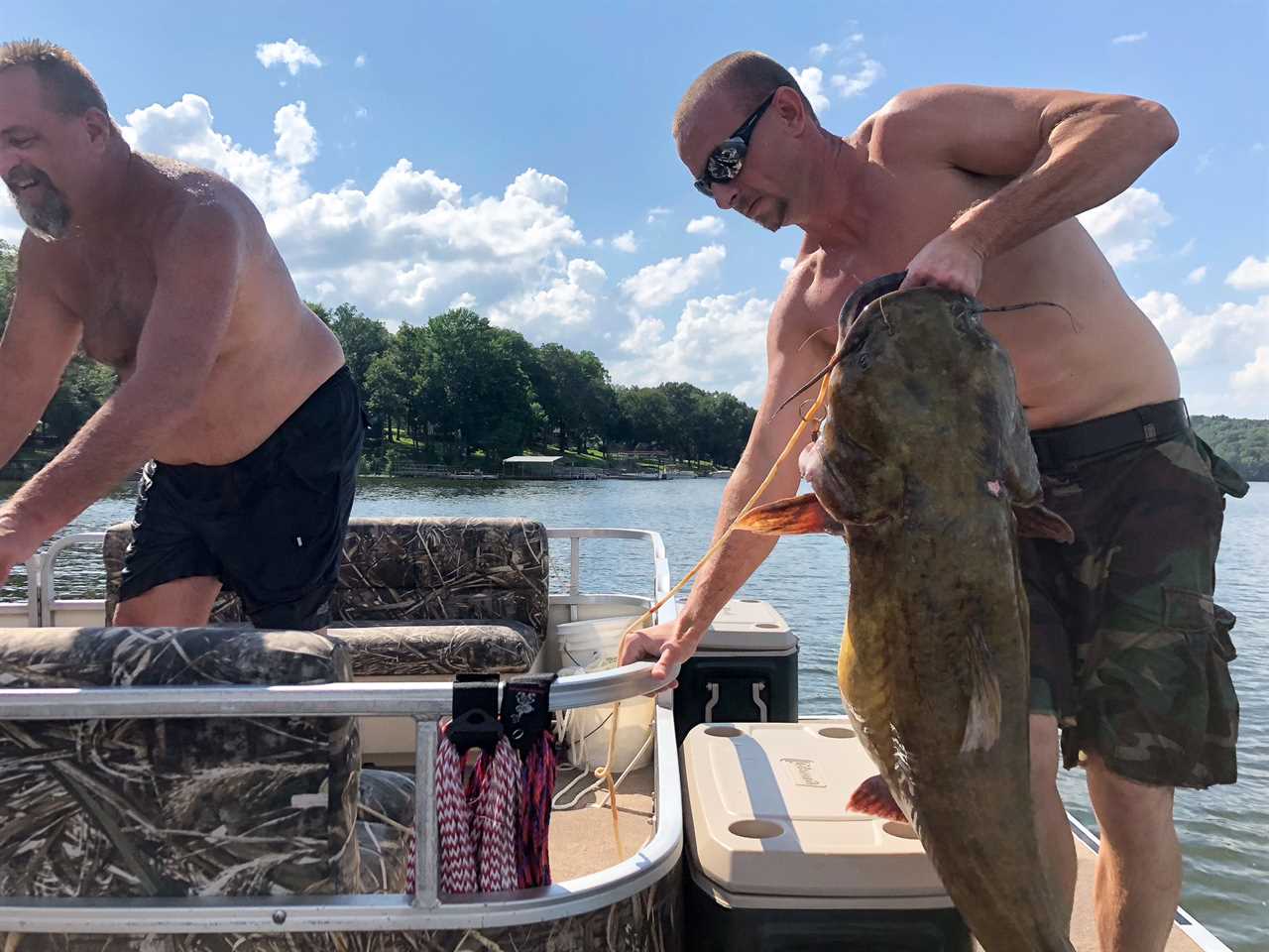 A man holds up a flathead on a pontoon boat.